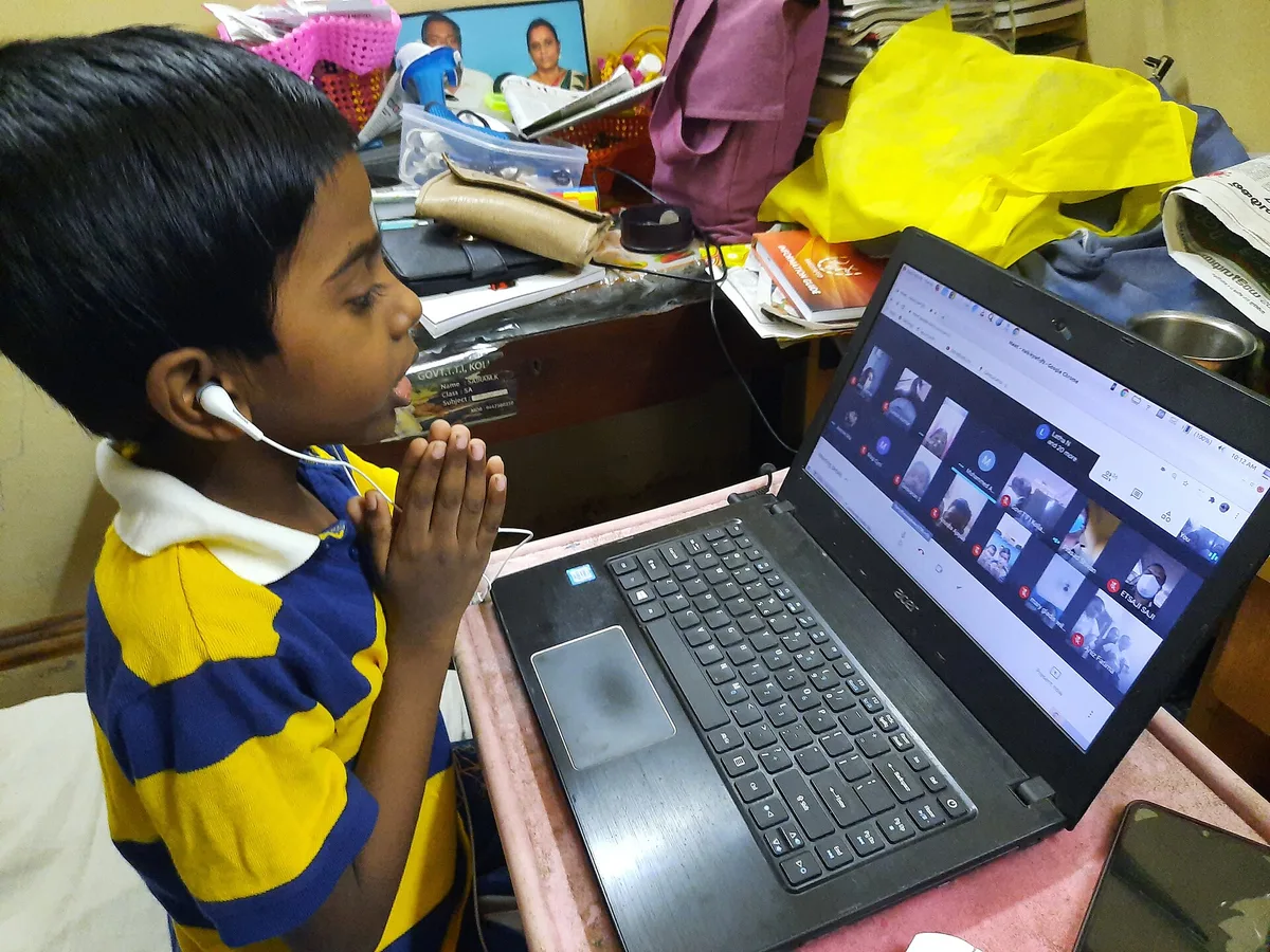 Menino de mãos postas participa de aula on-line em videochamada com vários participantes no laptop