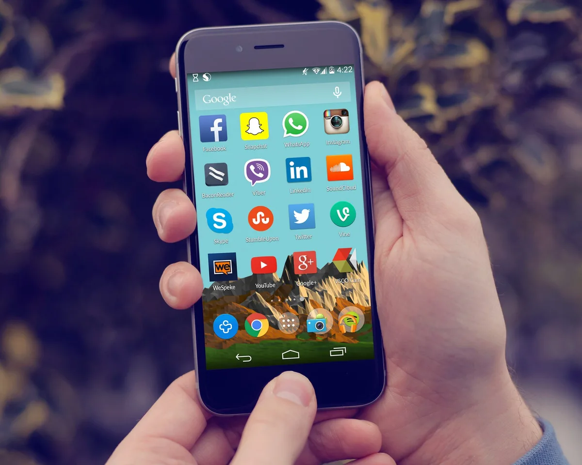 Mãos segurando um celular com ícones de aplicativos de redes sociais na tela