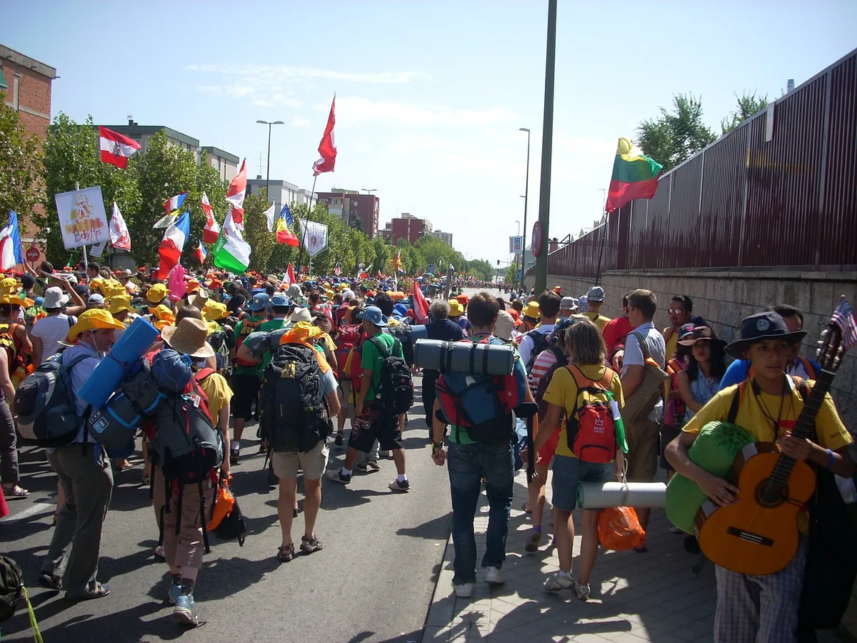 Jovens peregrinos de vários países caminham com mochilas e bandeiras em uma rua durante a Jornada Mundial da Juventude