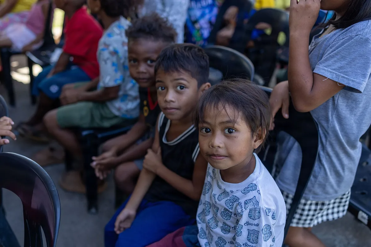 Crianças sentadas em cadeiras durante uma ação de Natal com doação de presentes para a comunidade