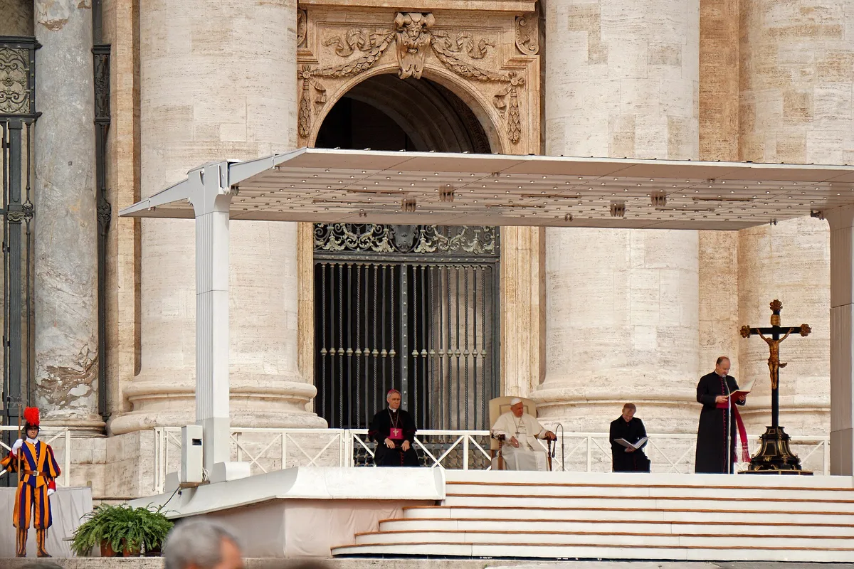 Audiência Geral na Praça São Pedro, com o papa sob o dossel, leitor ao lado do crucifixo e guarda suíço