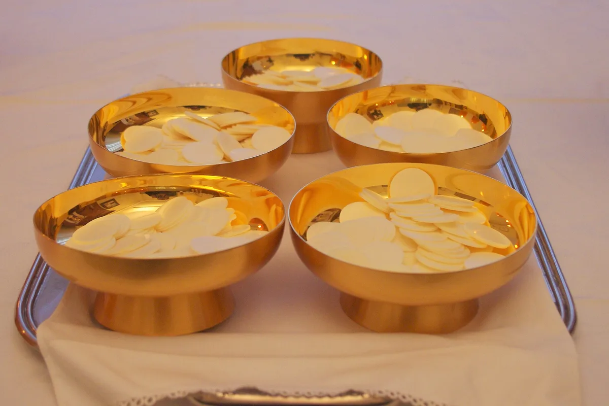 Patenas douradas com hóstias para a comunhão, sobre uma bandeja com toalha branca