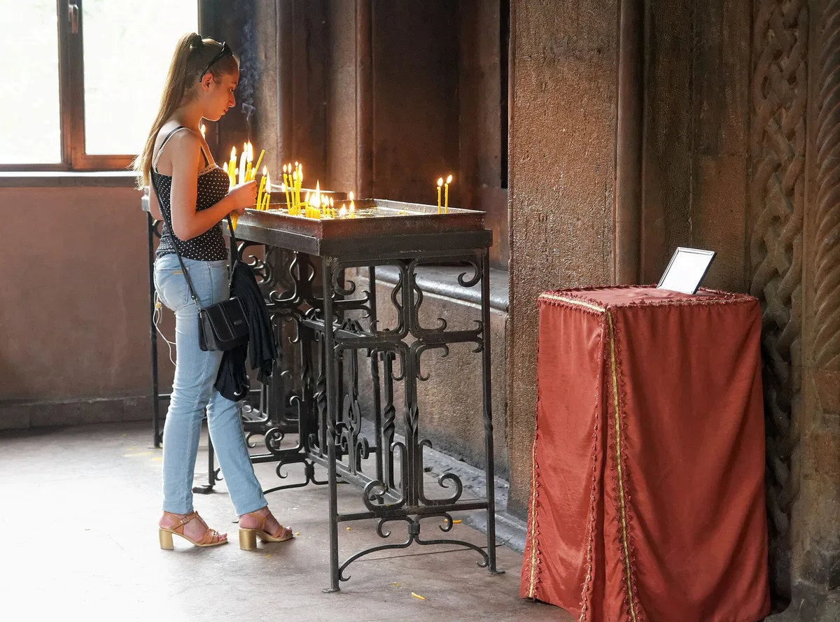 Jovem acendendo uma vela em suporte de ferro dentro de uma igreja de pedra