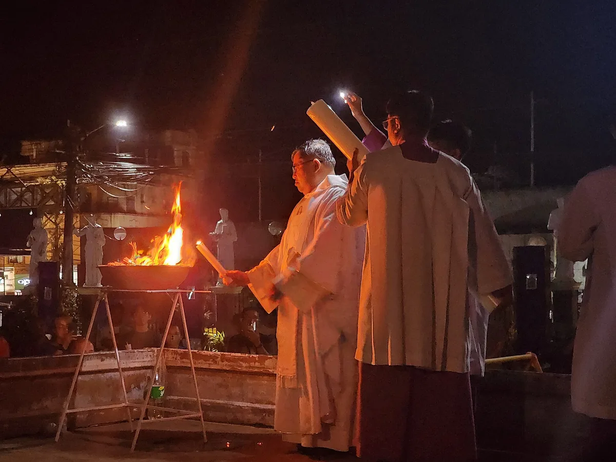 Padres ao redor do fogo novo à noite, com o círio pascal, no início da Vigília Pascal